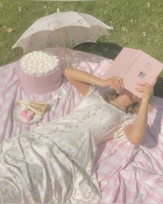 a woman laying on top of a pink blanket next to an umbrella and popcorn bucket