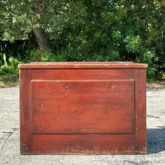 an old wooden box sitting in the middle of a parking lot next to some trees