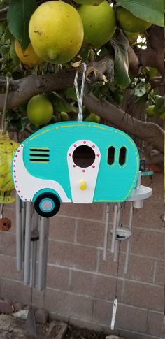 a blue and white camper shaped birdhouse hanging from a tree with fruit in the background