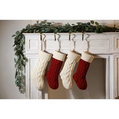 three stockings hanging from a mantel decorated with greenery