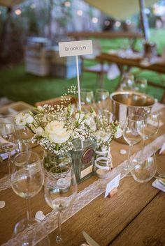 a wooden table topped with lots of wine glasses and vases filled with white flowers