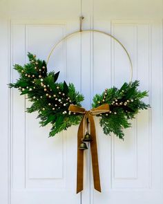 a christmas wreath hanging on the front door with bells and greenery around it's edges