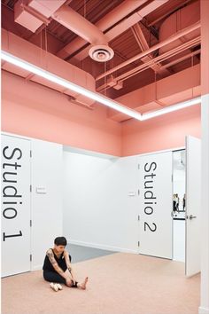 a woman sitting on the floor in an empty room with two doors and pink walls