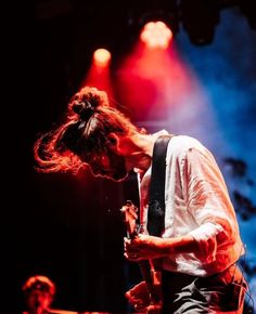 a man with long hair playing an electric guitar in front of red and blue lights