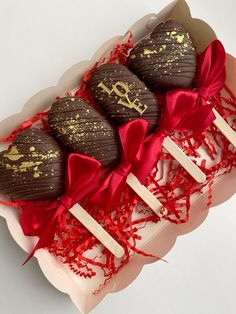 three chocolate covered lollipops in a box with red ribbon and bow on top