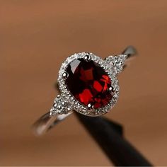 a red and white diamond ring sitting on top of a black piece of wood in front of a brown background