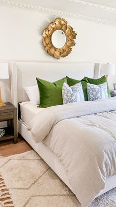 a bed with white sheets and green pillows in a small room next to a mirror