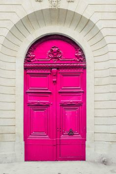 a bright pink door in front of a white brick building with an arch above it