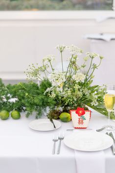 an arrangement of flowers and fruit on a white table cloth set for a formal dinner