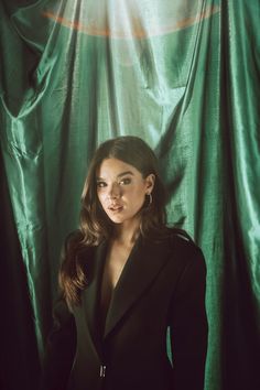 a woman standing in front of a green curtain with her hands on her hips and looking at the camera