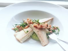 a white plate topped with meat and veggies next to a fork on a window sill