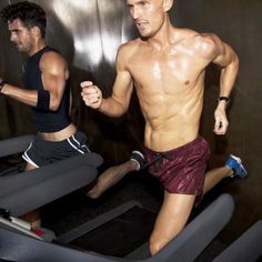 two men running on treadmills in a gym area, one is shirtless