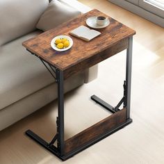 a small wooden table with a plate of fruit on it next to a gray couch