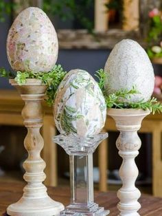 three wooden candlesticks with painted easter eggs on them sitting on a table in front of a fireplace