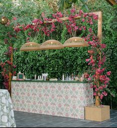 an outdoor bar with pink flowers and greenery on the wall, surrounded by plants