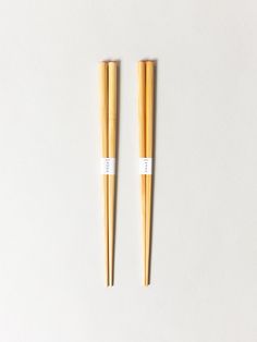 two wooden chopsticks sitting next to each other on a white surface with one stick sticking out of it