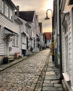 a cobblestone street lined with white wooden houses and lampposts on either side