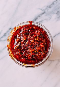 a glass bowl filled with red sauce on top of a marble counter