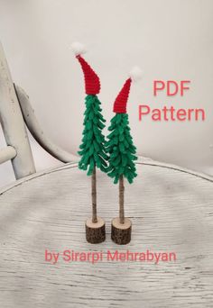 two knitted trees with red and green hats on them sitting on top of a wooden table