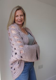 a woman standing in front of a wall wearing a pink cardigan sweater and jeans