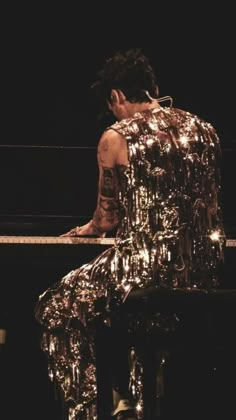 a man sitting on top of a piano covered in lots of shiny silver foils