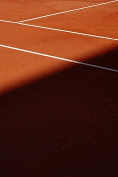 the shadow of a tennis player is cast on an orange clay court with white lines