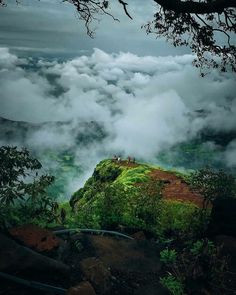 people standing on top of a green hill surrounded by clouds and greenery in the distance