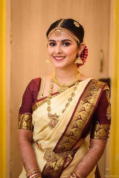 a woman in a white and red sari with gold jewelry on her head, smiling