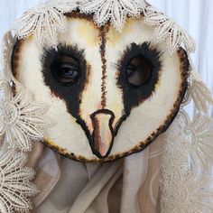 an owl mask with white lace on it's head and eyes, sitting on top of a cloth