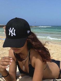 a woman laying on top of a beach next to the ocean wearing a yankees hat