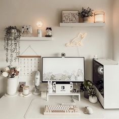 a desk with a monitor, keyboard and mouse on it in front of some plants