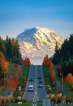 cars are driving down the road in front of a snow covered mountain with trees on both sides