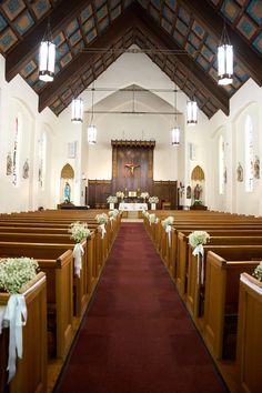 an empty church filled with pews and decorated with flowers on the aisle, in front of two rows of pews