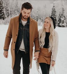 a man and woman walking in the snow holding hands