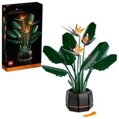 an artificial plant in a black pot next to a cardboard box with the image of a bird of paradise on it