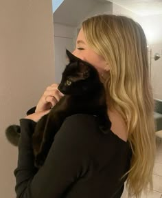 a woman is holding a black cat in her arms and looking at the mirror behind her