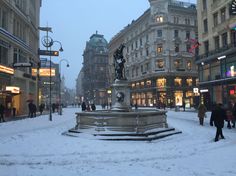 people are walking around in the snow on a city street with tall buildings and shops