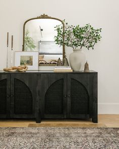 a black sideboard with three doors and a mirror on top in front of it