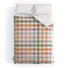 a bed with two pillows on top of it next to a pillow case that has an orange, white and green checkered pattern