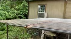 a house with a metal roof next to a fence and trees in the back yard