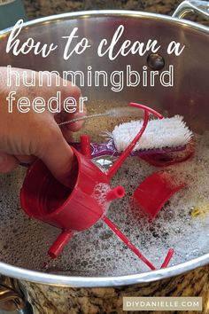 a person is cleaning a bird feeder with a red brush and sponges in it