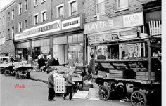 an old black and white photo of people walking down the street in front of stores