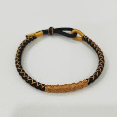 a black and gold braided bracelet on a white surface with an orange bead cord