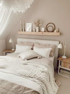 a white bed sitting under a window next to a wooden shelf filled with pictures and candles