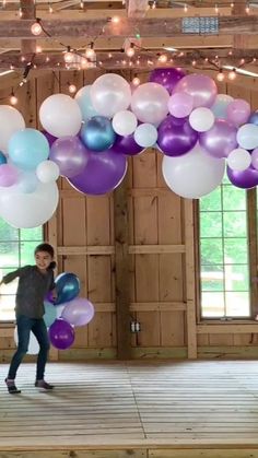 a young boy holding balloons while standing on a wooden floor in front of a building