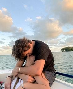 a man and woman kissing while sitting on a boat in the ocean at sunset or dawn