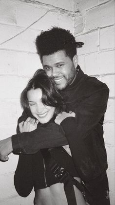 a man and woman hugging each other in front of a brick wall