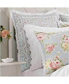 a bed topped with lots of pillows covered in pink and white flowers next to a night stand