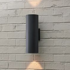 two lights on the side of a white brick wall next to a black lamp fixture