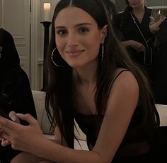 a woman sitting on a couch holding a cell phone in her hand and looking at the camera